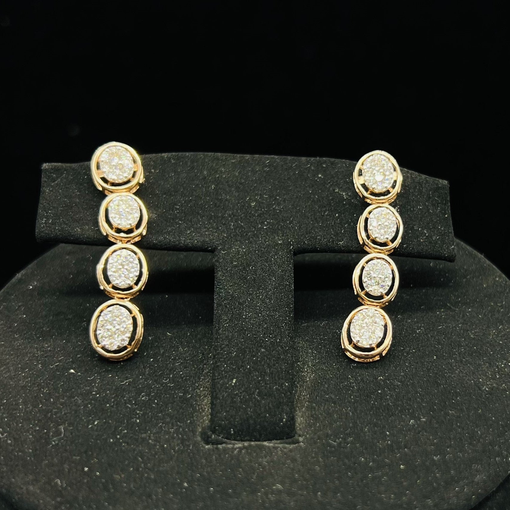 Gold diamond earrings set featuring oval-shaped, pavé-set diamonds in rose gold. The earrings has a linked design showcasing these sparkling stones evenly spaced. Earrings mirror the necklace stones in a vertical stack, creating an elegant accessory set on a black velvet background.