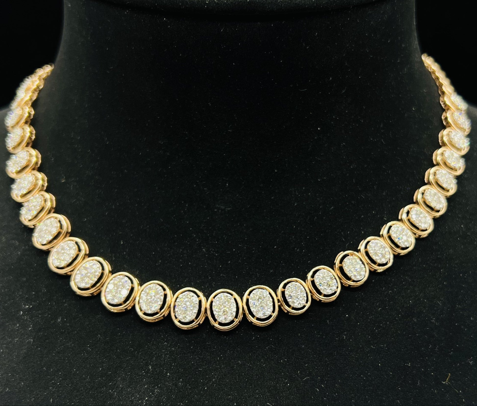 Gold diamond necklace set featuring oval-shaped, pavé-set diamonds in rose gold. The necklace has a linked design showcasing these sparkling stones evenly spaced on a black velvet background.