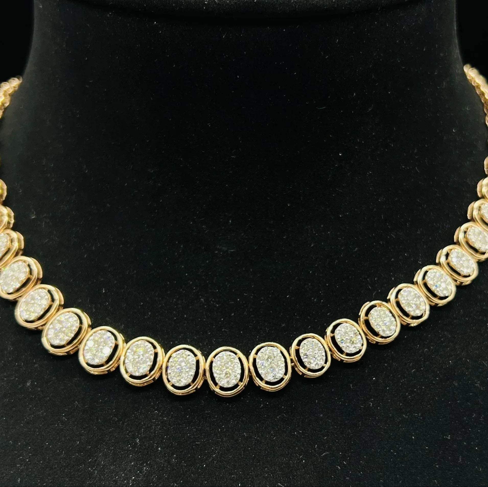 Gold diamond necklace set featuring oval-shaped, pavé-set diamonds in rose gold. The necklace has a linked design showcasing these sparkling stones evenly spaced on a black velvet background.