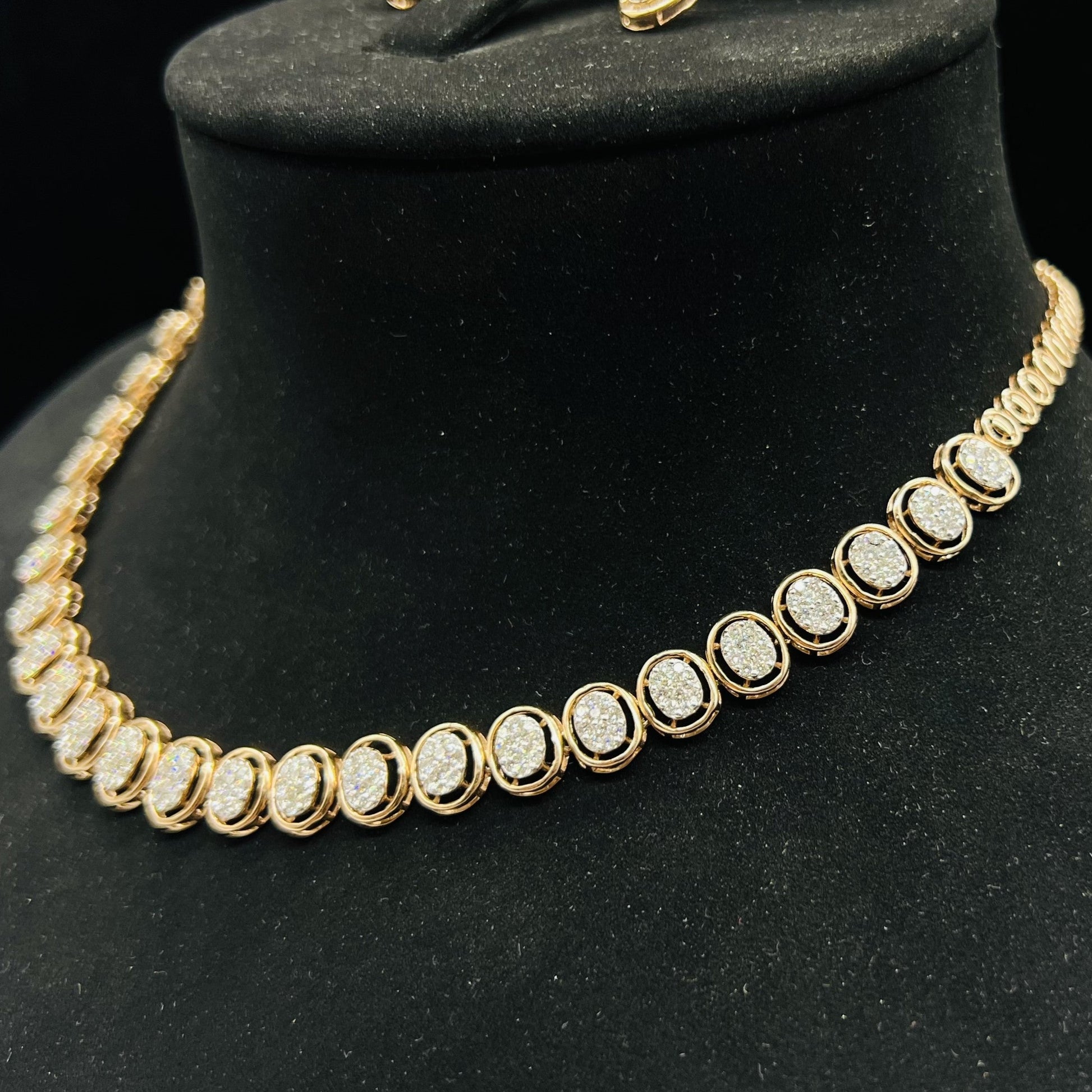 Gold diamond necklace set featuring oval-shaped, pavé-set diamonds in rose gold. The necklace has a linked design showcasing these sparkling stones evenly spaced on a black velvet background.