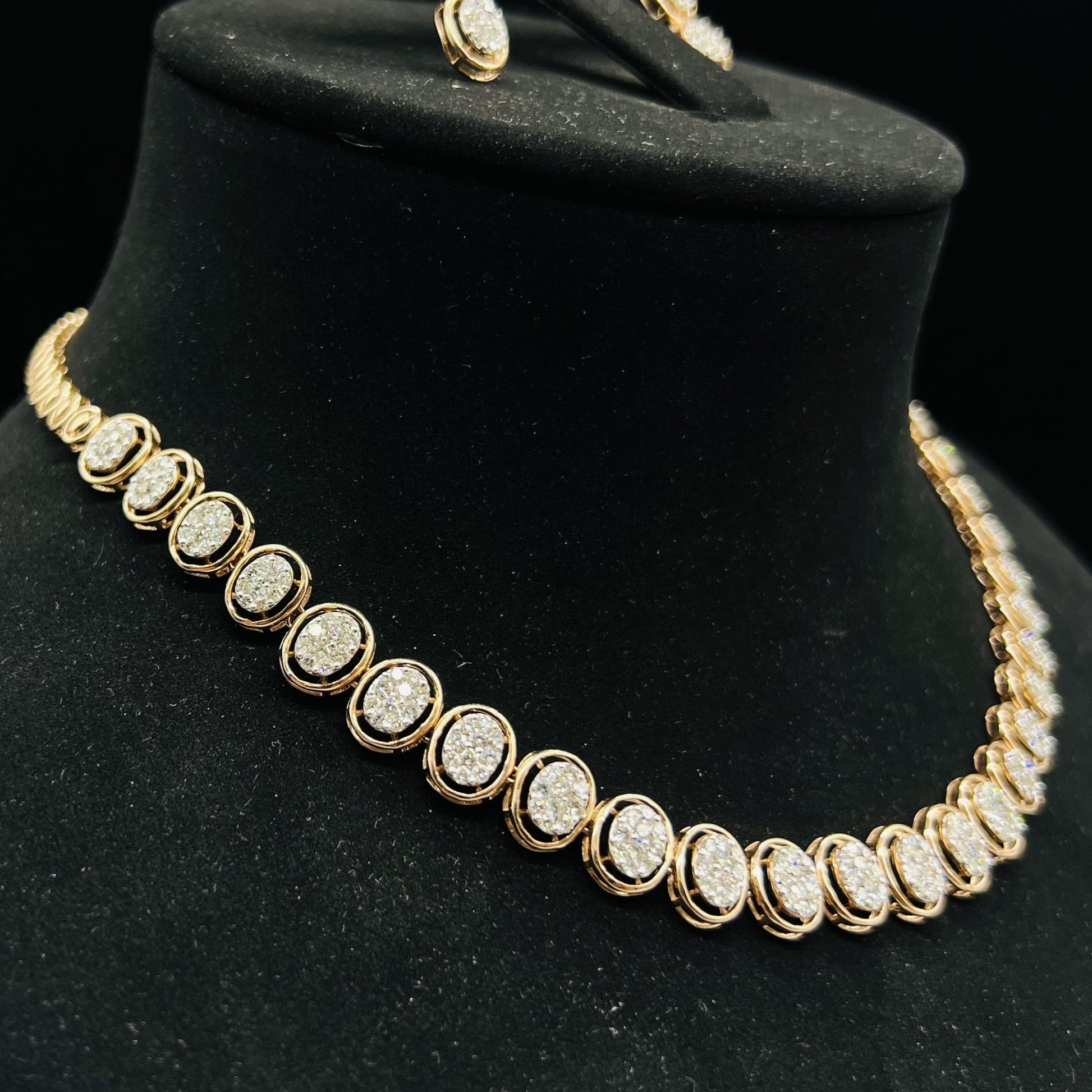Gold diamond necklace set featuring oval-shaped, pavé-set diamonds in rose gold. The necklace has a linked design showcasing these sparkling stones evenly spaced on a black velvet background.