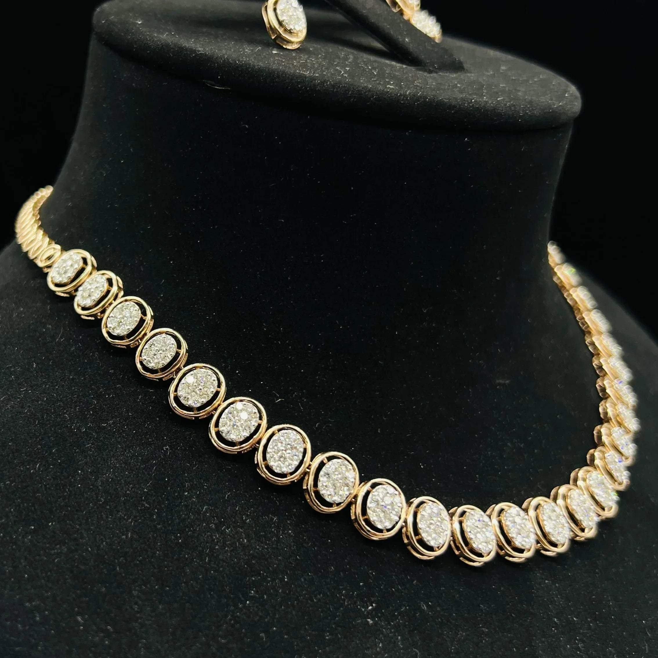 Gold diamond necklace set featuring oval-shaped, pavé-set diamonds in rose gold. The necklace has a linked design showcasing these sparkling stones evenly spaced on a black velvet background.
