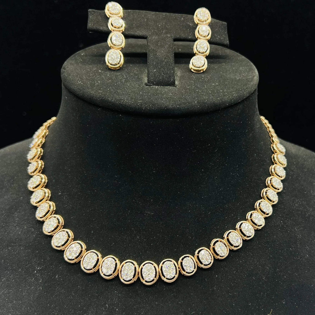 Gold diamond necklace set with matching earrings featuring oval-shaped, pavé-set diamonds in rose gold. The necklace has a linked design showcasing these sparkling stones evenly spaced. Earrings mirror the necklace stones in a vertical stack, creating an elegant accessory set on a black velvet background.