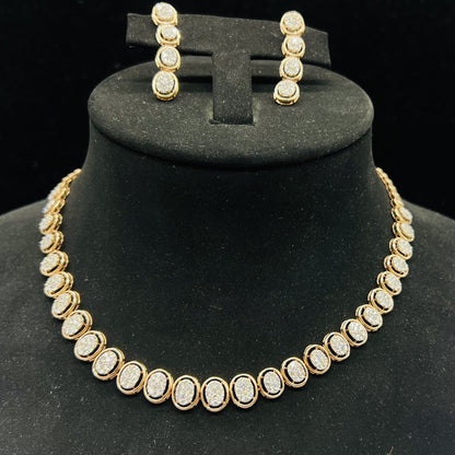 Gold diamond necklace set with matching earrings featuring oval-shaped, pavé-set diamonds in rose gold. The necklace has a linked design showcasing these sparkling stones evenly spaced. Earrings mirror the necklace stones in a vertical stack, creating an elegant accessory set on a black velvet background.