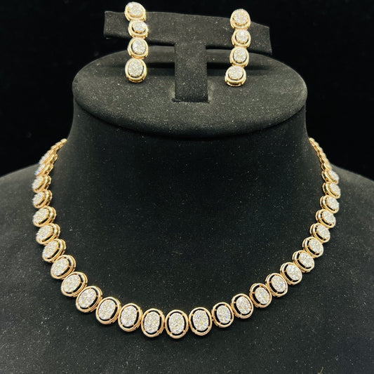 Gold diamond necklace set with matching earrings featuring oval-shaped, pavé-set diamonds in rose gold. The necklace has a linked design showcasing these sparkling stones evenly spaced. Earrings mirror the necklace stones in a vertical stack, creating an elegant accessory set on a black velvet background.