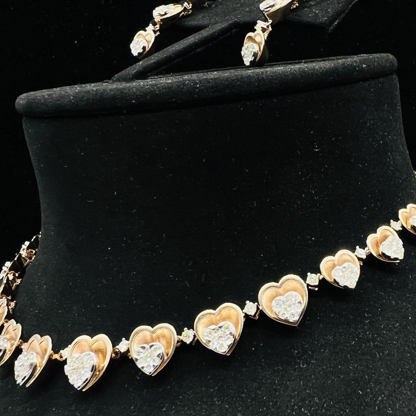A gold necklace with round-cut diamond pendants and coordinating earrings, displayed on a black mannequin bust.