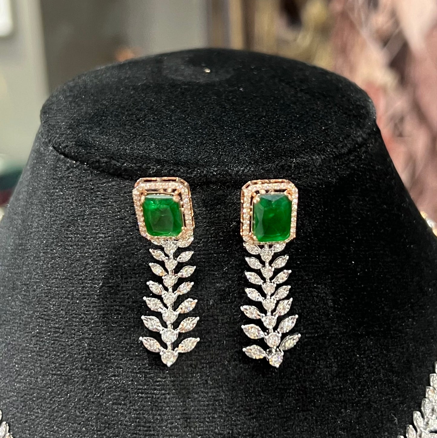 Diamond earrings set featuring a radiant emerald centerpiece framed by diamond leaves and cascading diamond drops on a black background.