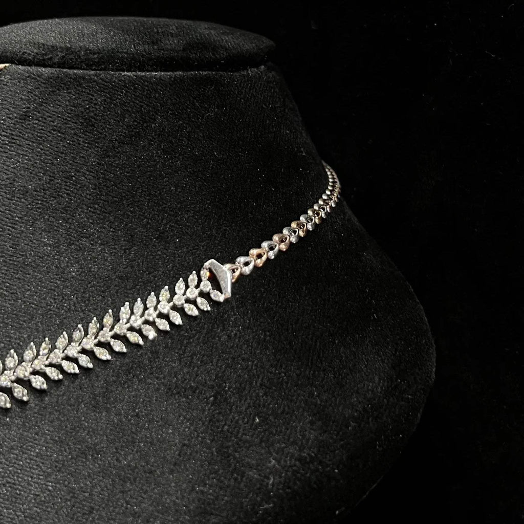Diamond necklace set framed by diamond leaves and cascading diamond drops on a mannequin bust from left side.