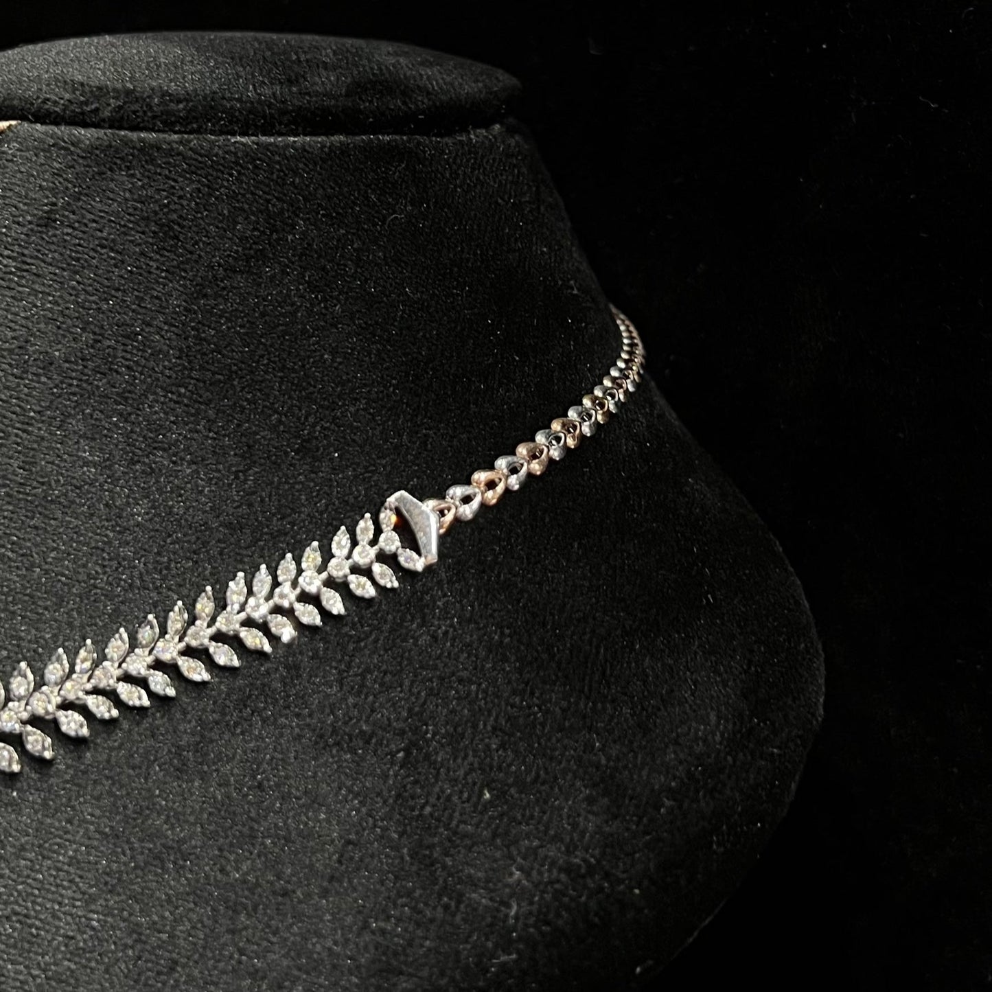 Diamond necklace set framed by diamond leaves and cascading diamond drops on a mannequin bust from left side.