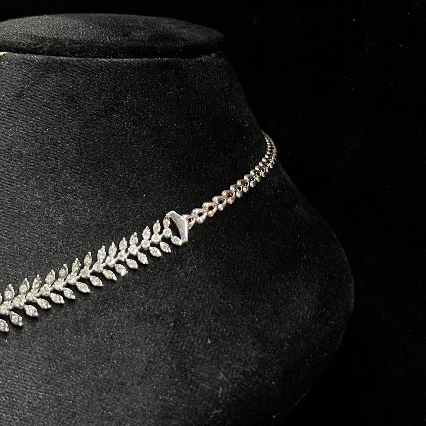 Diamond necklace set framed by diamond leaves and cascading diamond drops on a mannequin bust from left side.