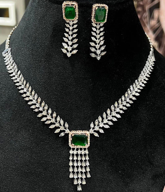 Diamond necklace set featuring a radiant green color stone centerpiece framed by diamond leaves and cascading diamond drops, paired with matching earrings on a mannequin bust.