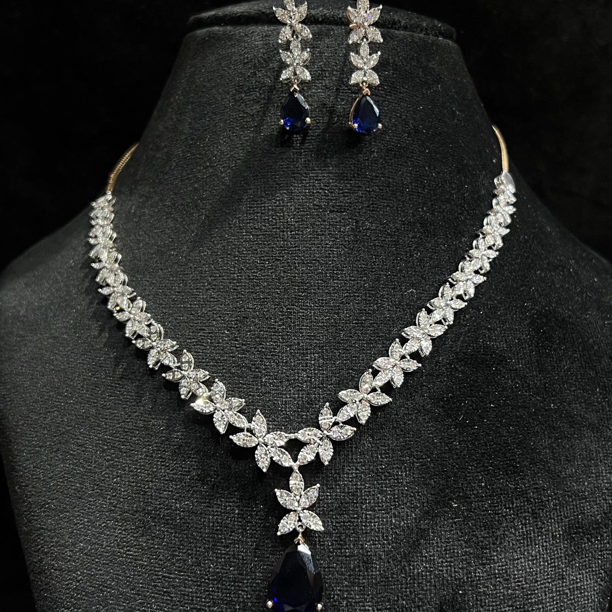 Diamond necklace set with color stone drop pendant and matching floral diamond earrings displayed on black stand.