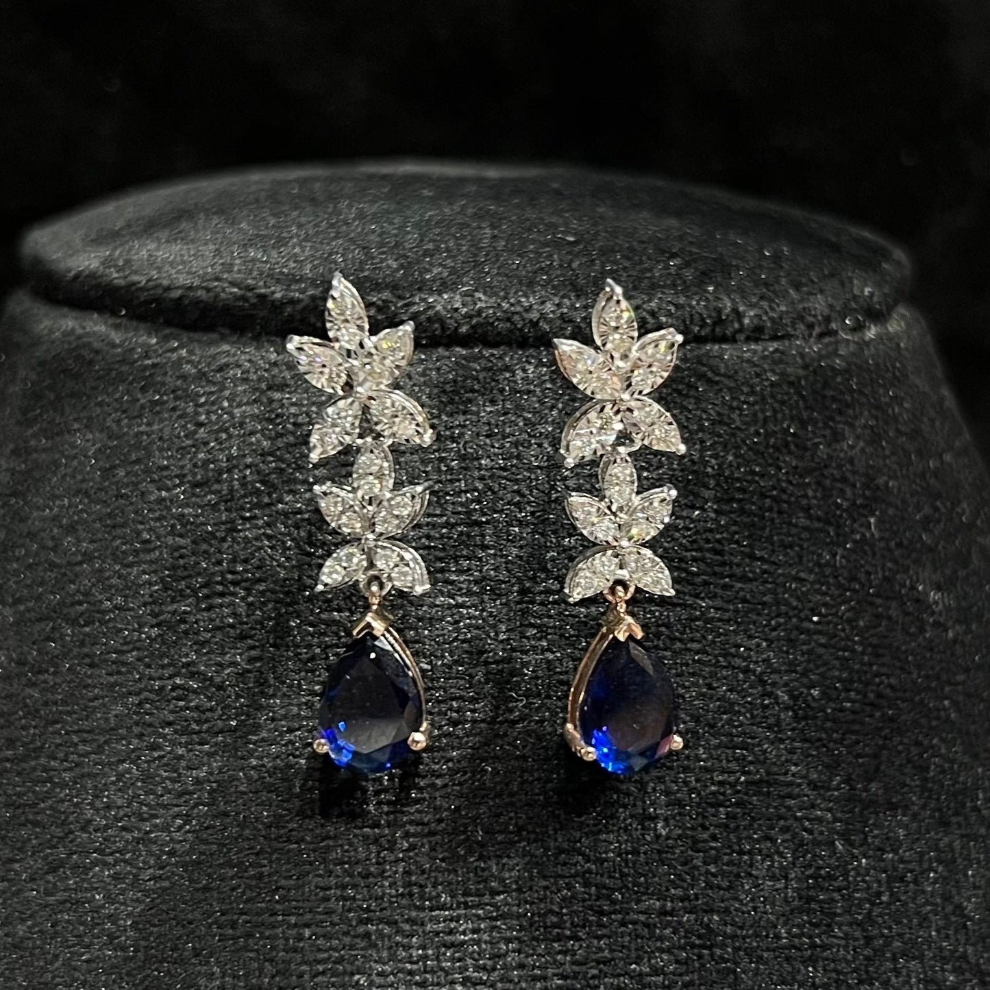 Close-up of diamond earrings set showing detailed floral design and pear-shaped color stone drop on a mannequin bust.