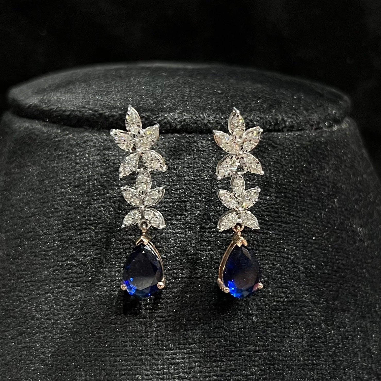 Close-up of diamond earrings set showing detailed floral design and pear-shaped color stone drop on a mannequin bust.