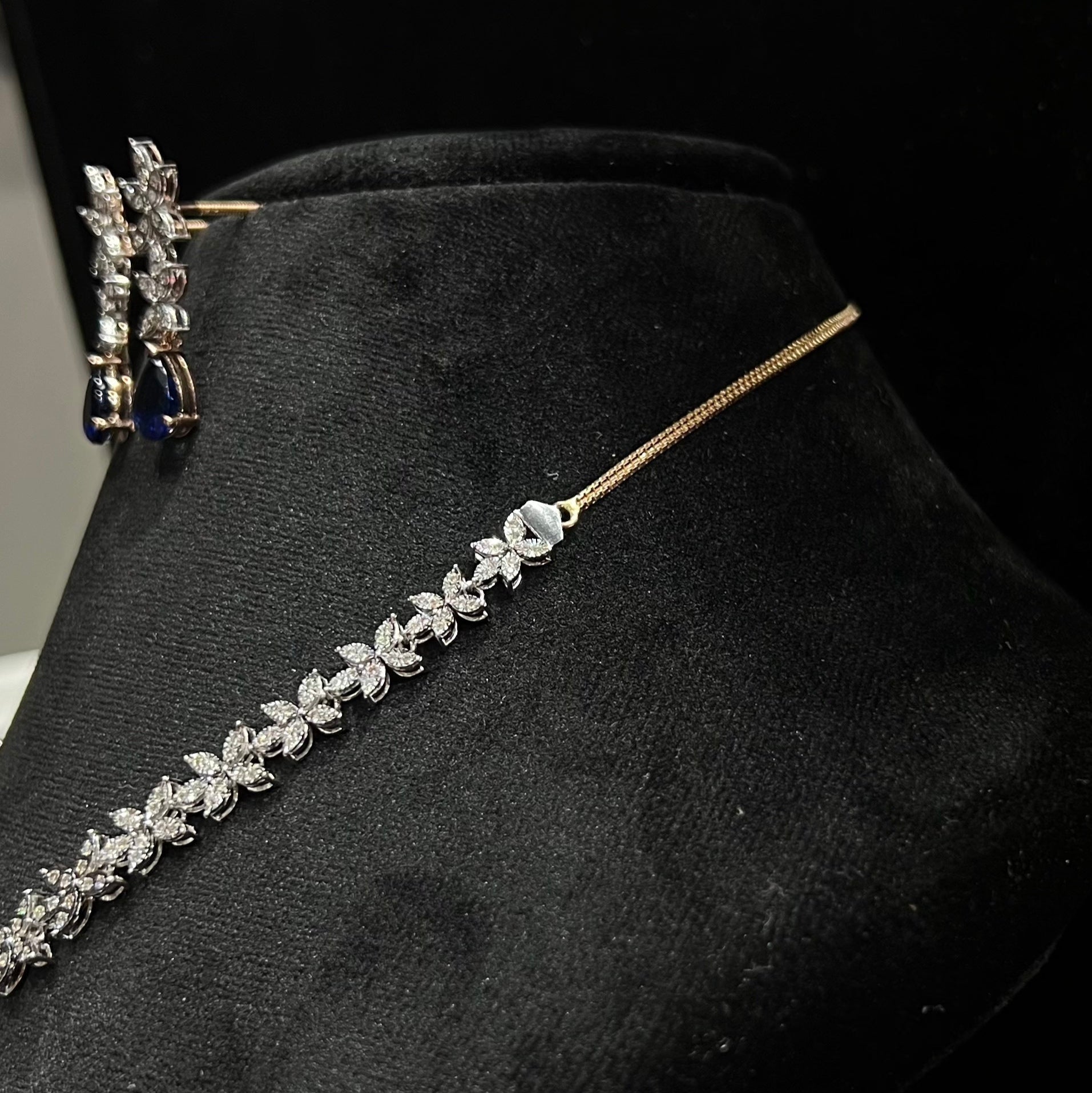 Diamond necklace set with color stone drop pendant and matching floral diamond earrings displayed on black stand from left side.