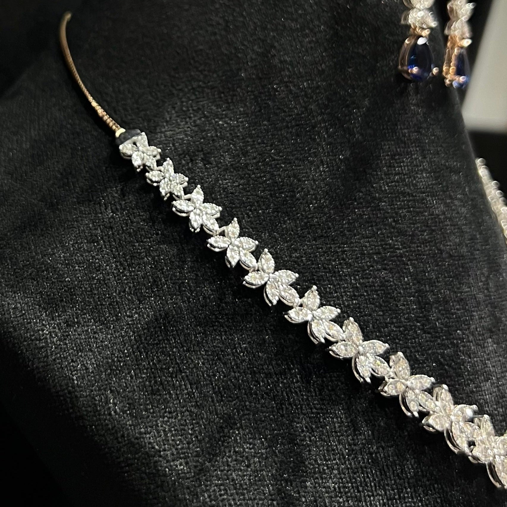 Diamond necklace set with color stone drop pendant and matching floral diamond earrings displayed on black stand from right side.