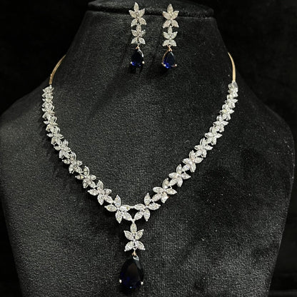 A gold diamond necklace set with matching earrings displayed on a mannequin bust, featuring a chain of gold and a series of graduated square and round cut diamonds & blue stones.