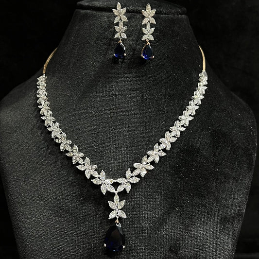 A gold diamond necklace set with matching earrings displayed on a mannequin bust, featuring a chain of gold and a series of graduated square and round cut diamonds & blue stones.