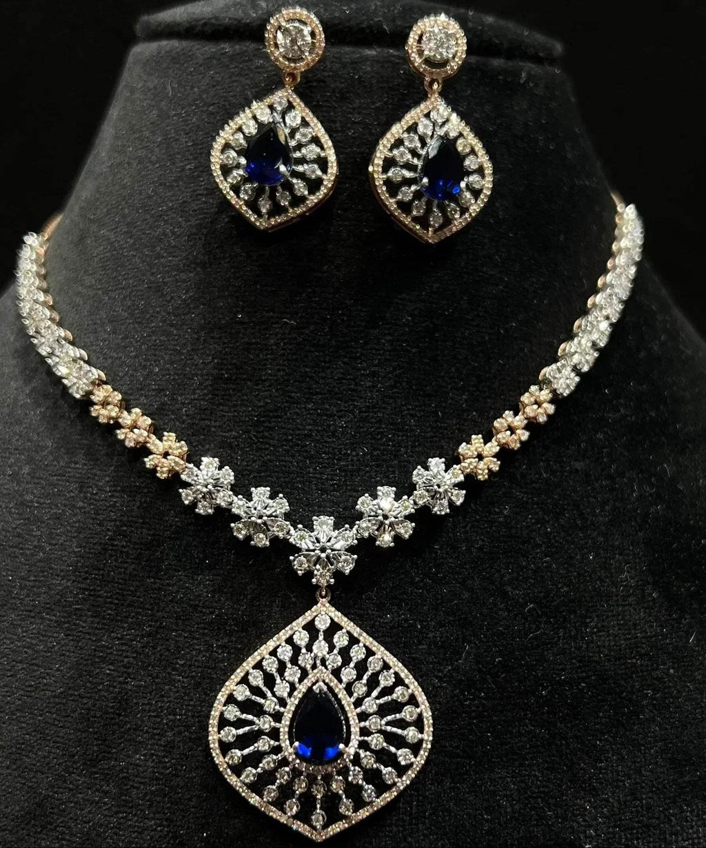 A gold diamond necklace with earrings, featuring a floral pattern and adorned with blue and clear stones.