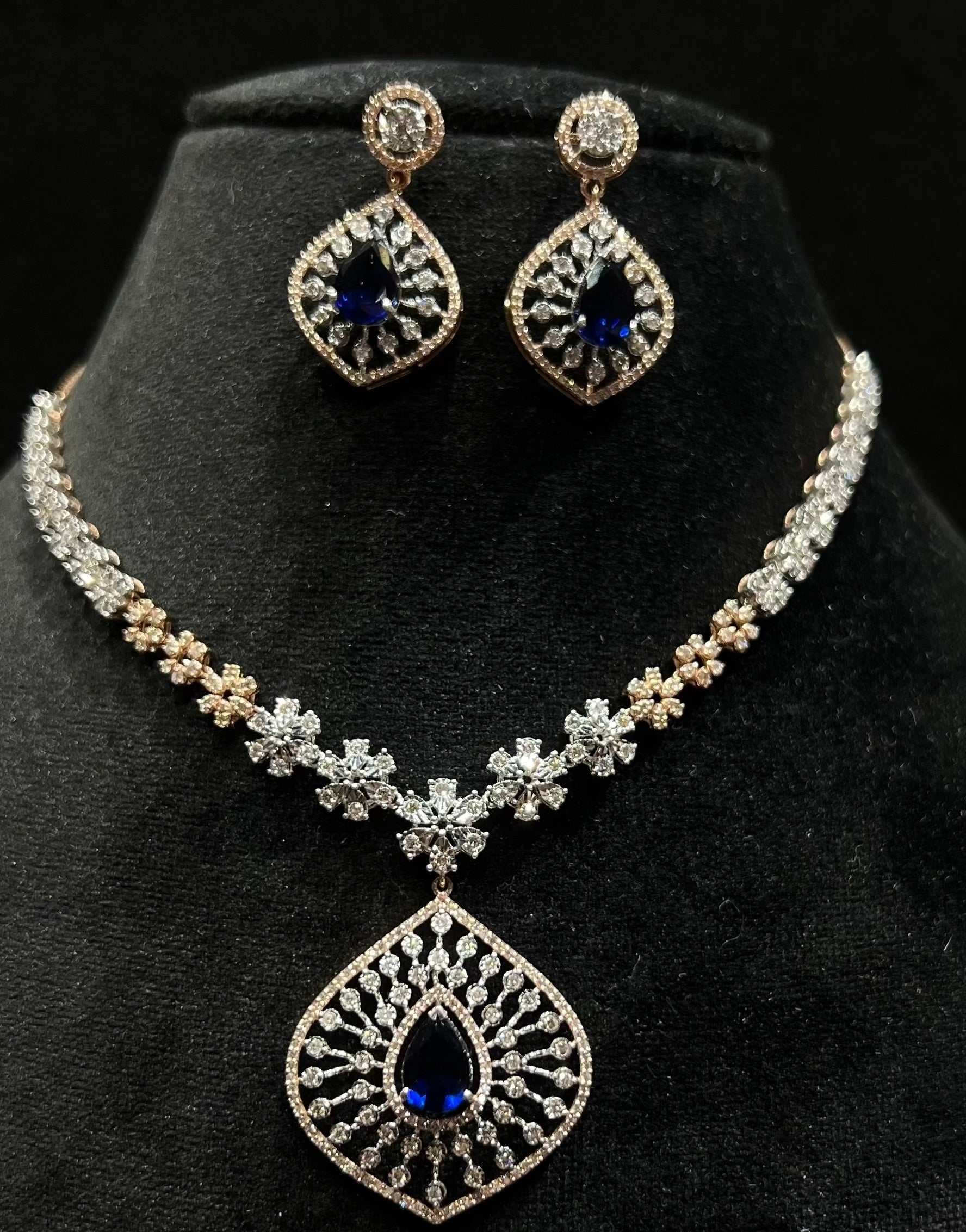 A gold diamond necklace with earrings, featuring a floral pattern and adorned with blue and clear stones.