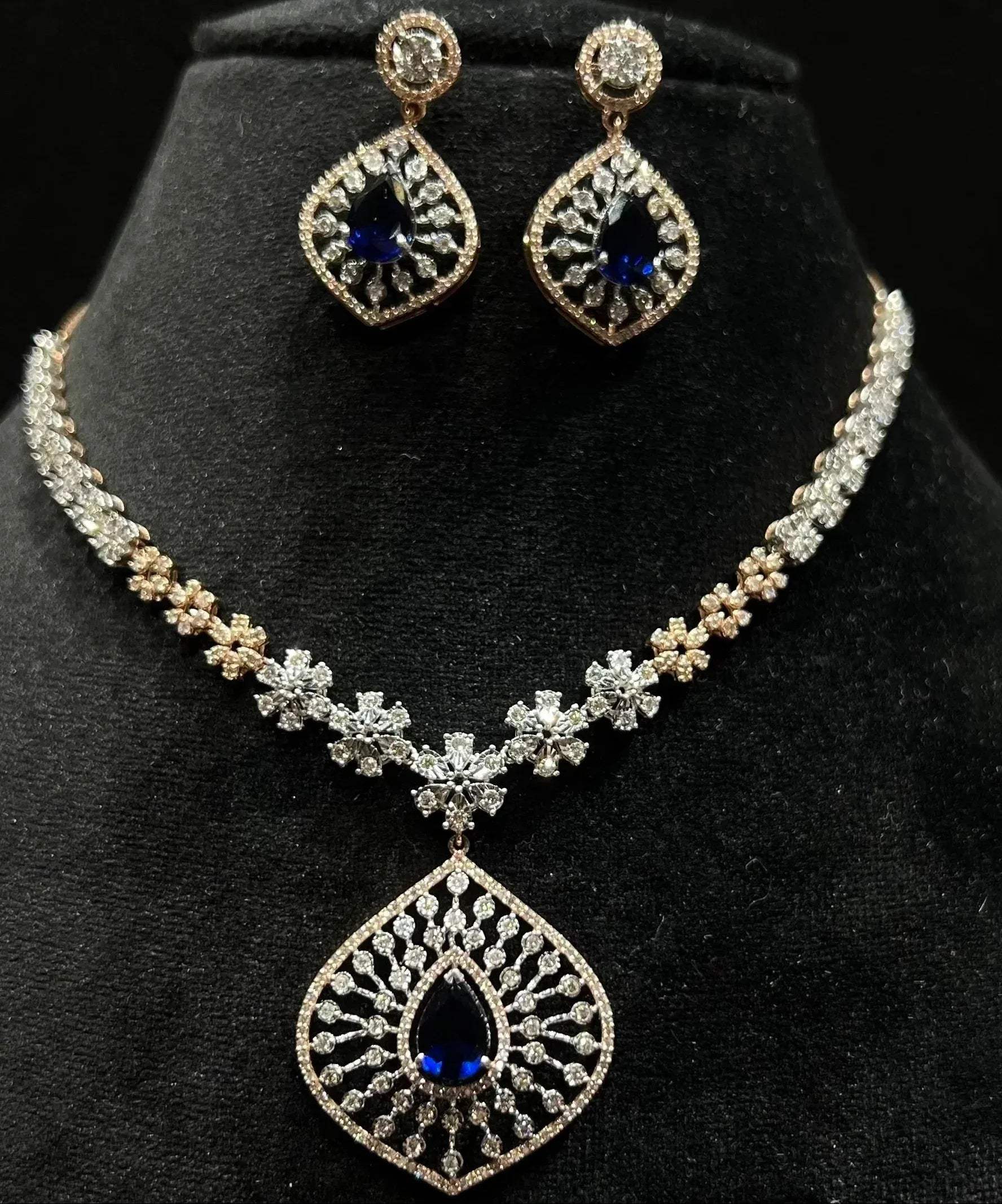 A gold diamond necklace with earrings, featuring a floral pattern and adorned with blue and clear stones.