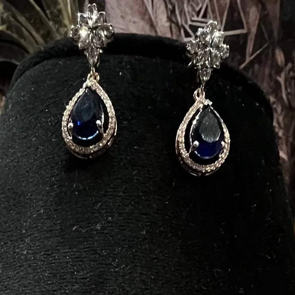 Elegant diamond necklace set with teardrop color stone pendant and matching earrings on black display