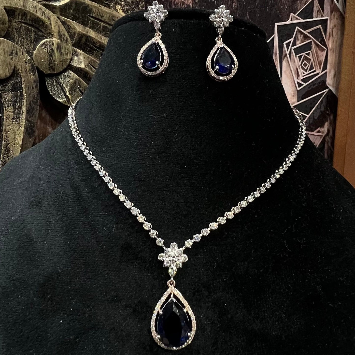 Elegant diamond necklace set with teardrop color stone pendant and matching earrings on black display