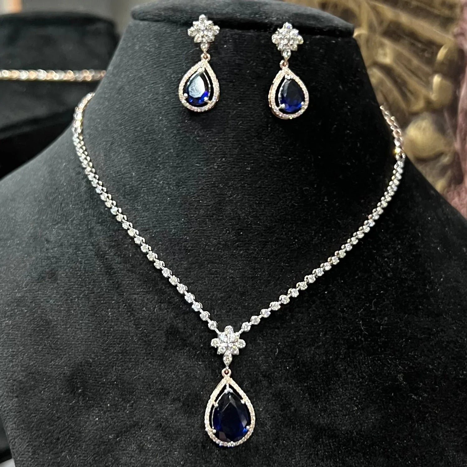 Elegant diamond necklace set with teardrop color stone pendant and matching earrings on black display
