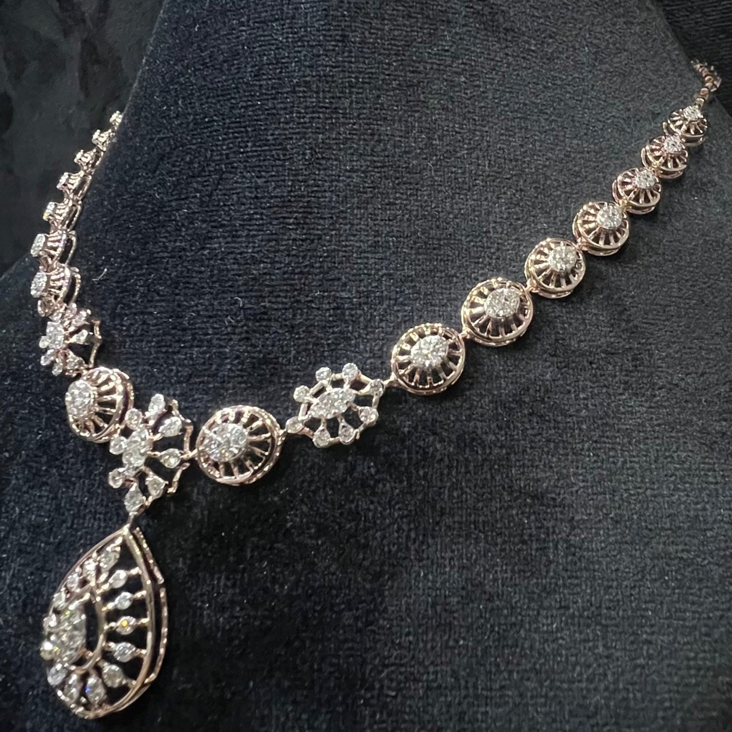 Elegant teardrop-shaped diamond necklace set with floral-inspired motifs displayed on a black background.