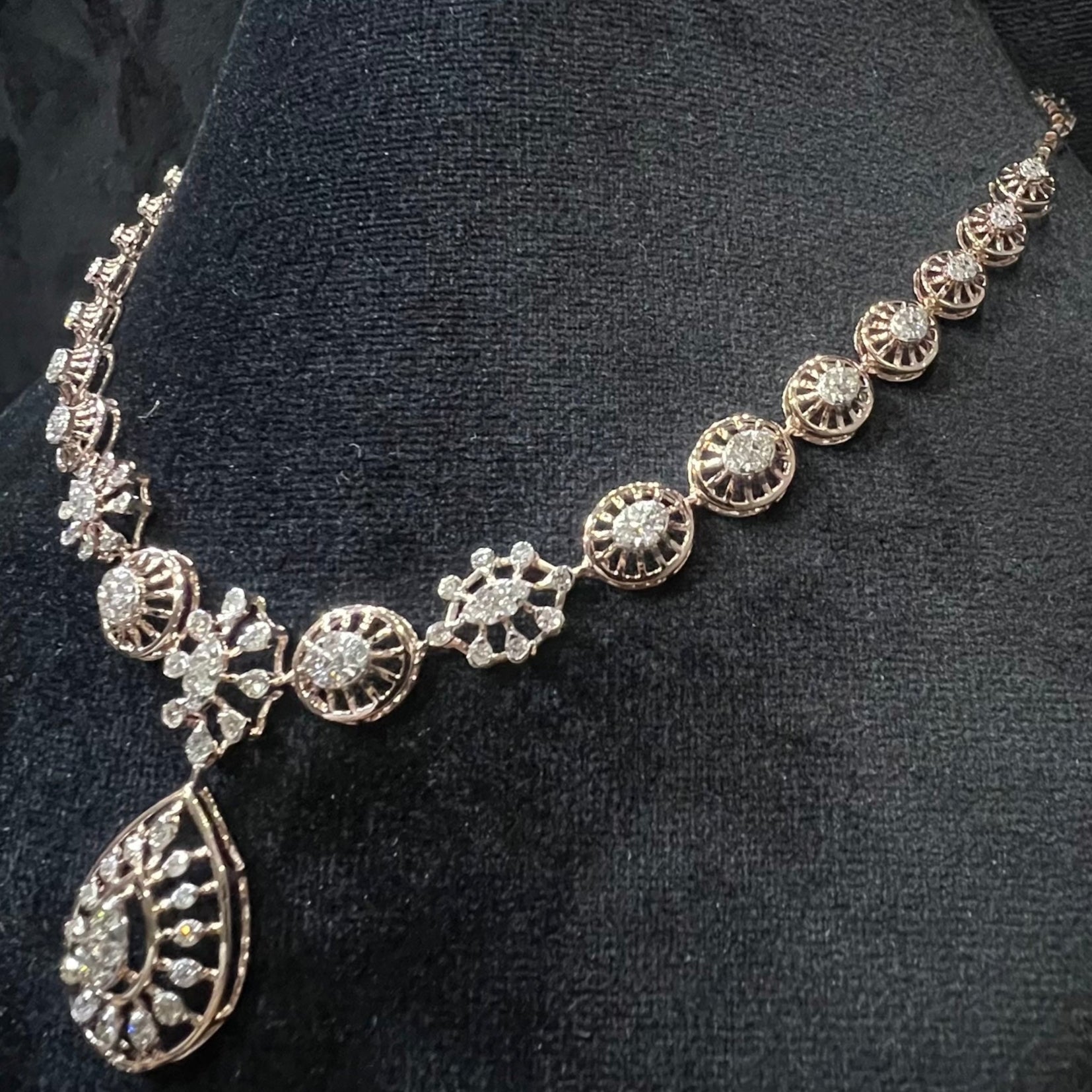 Elegant teardrop-shaped diamond necklace set with floral-inspired motifs displayed on a black background.