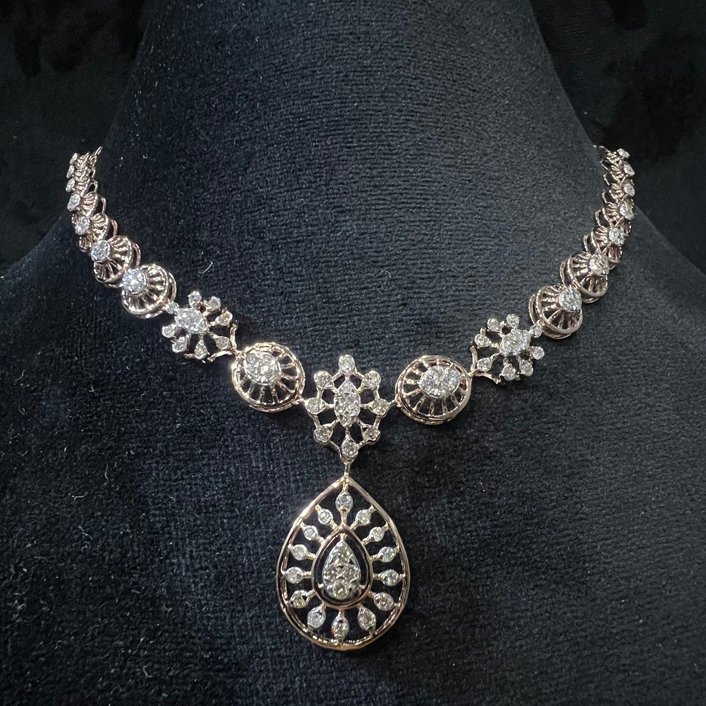 Elegant teardrop-shaped diamond necklace set with floral-inspired motifs displayed on a black background.