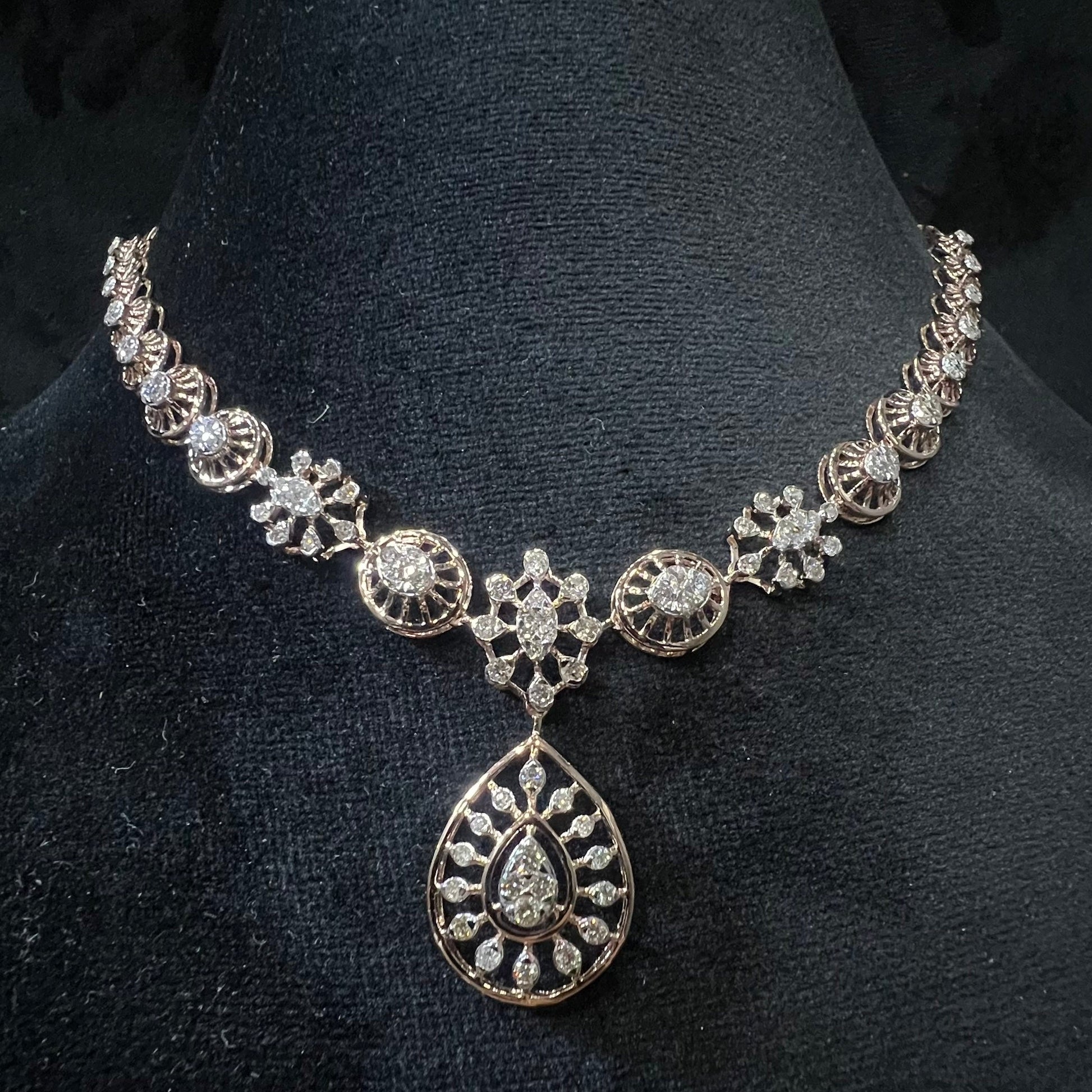 Elegant teardrop-shaped diamond necklace set with floral-inspired motifs displayed on a black background.