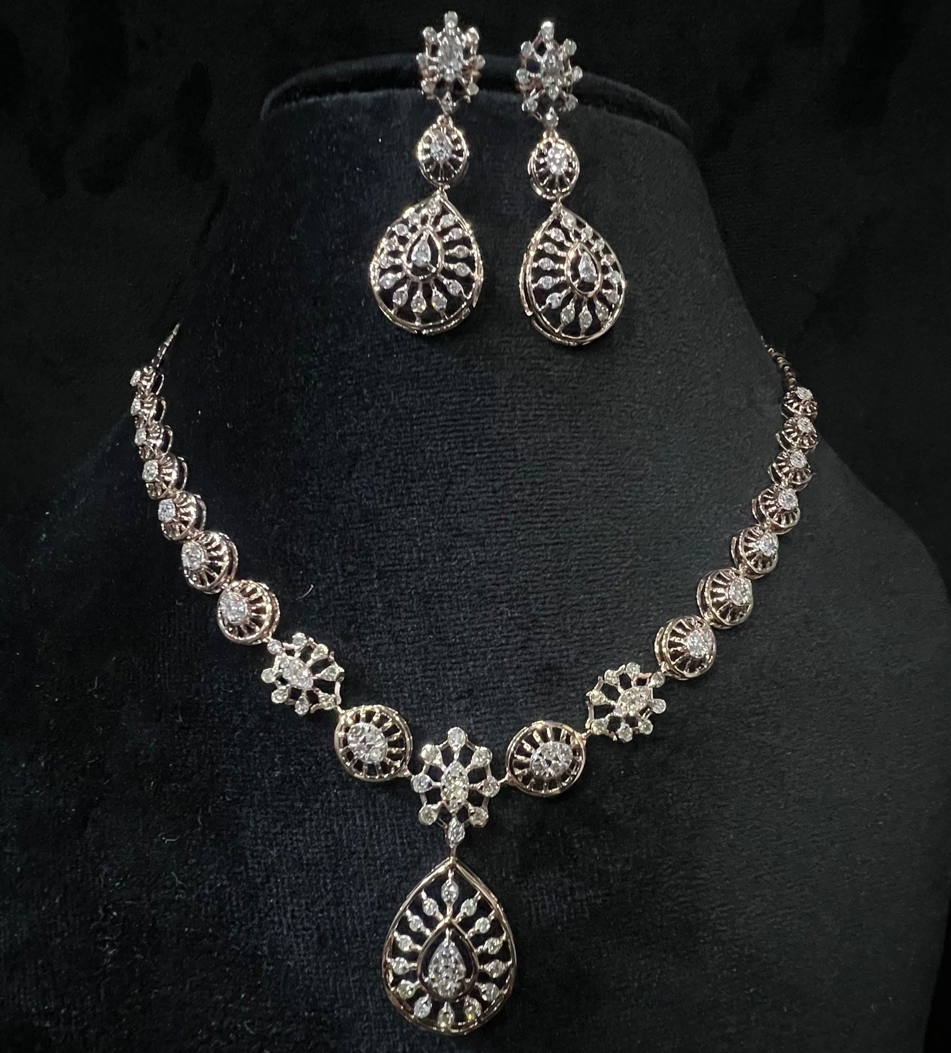 Elegant teardrop-shaped diamond necklace set with floral-inspired motifs and matching earrings displayed on a black background.