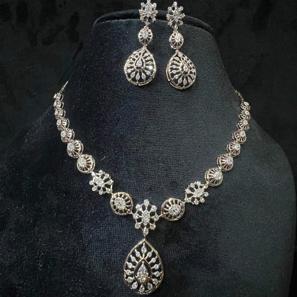 A gold diamond necklace with a floral pattern and a pair of matching earrings, displayed on a black mannequin bust.