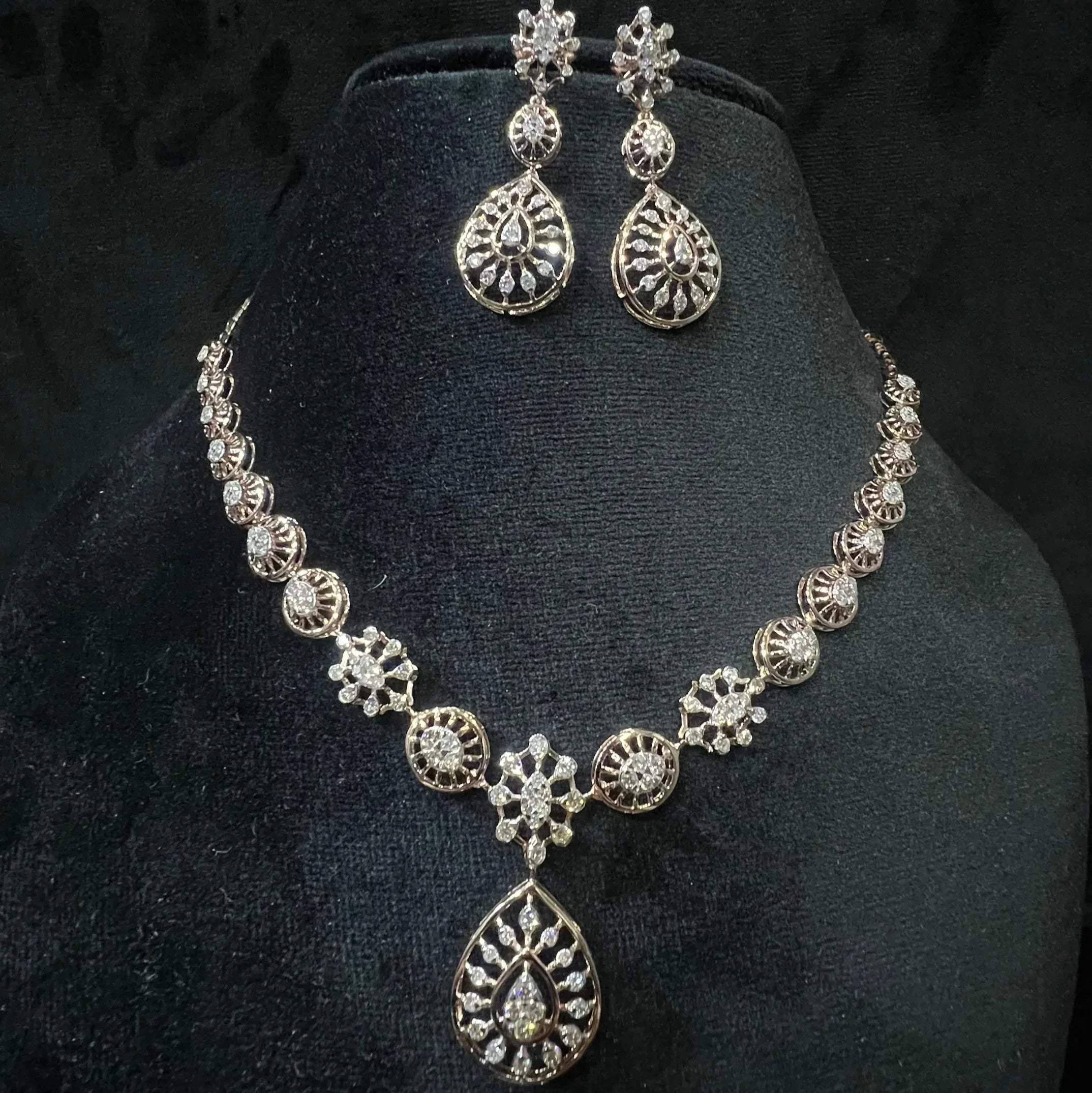 A gold diamond necklace with a floral pattern and a pair of matching earrings, displayed on a black mannequin bust.