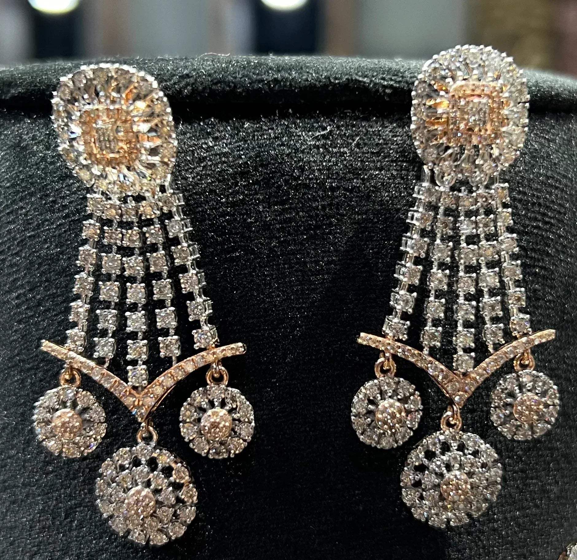 Close-up of luxurious diamond earrings featuring circular motifs and cascading diamond strands on a black display stand.