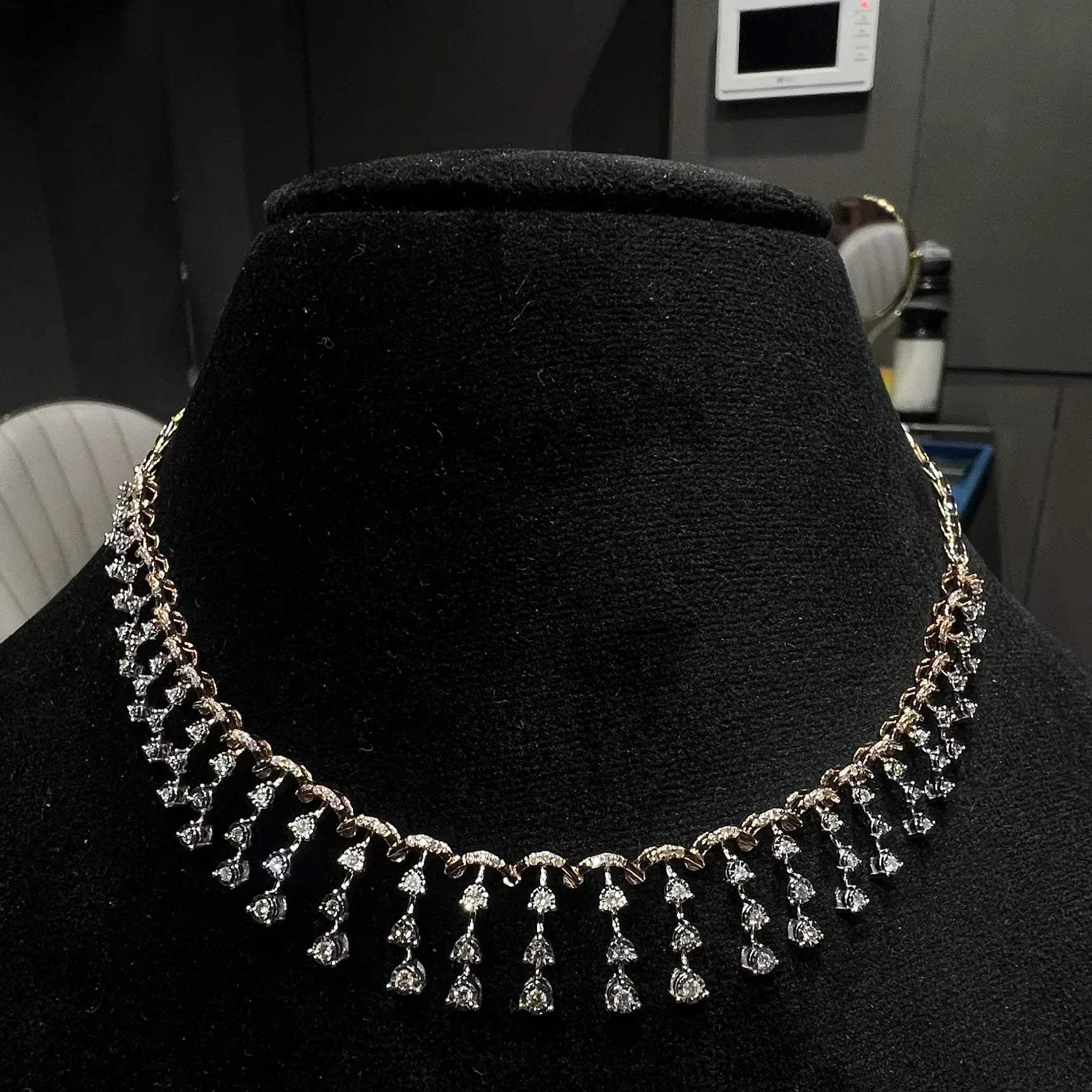 A gold diamond necklace attached to the neckline, set on a black mannequin.