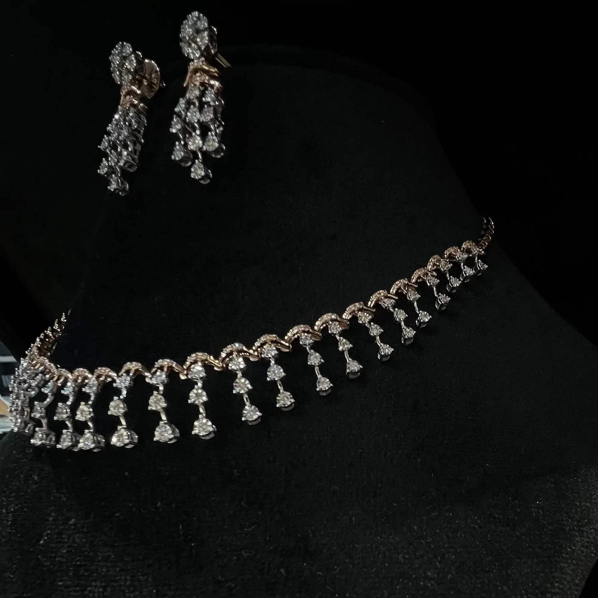 A gold diamond necklace with a series of round and marquise shaped earrings attached to the neckline, set on a black mannequin.