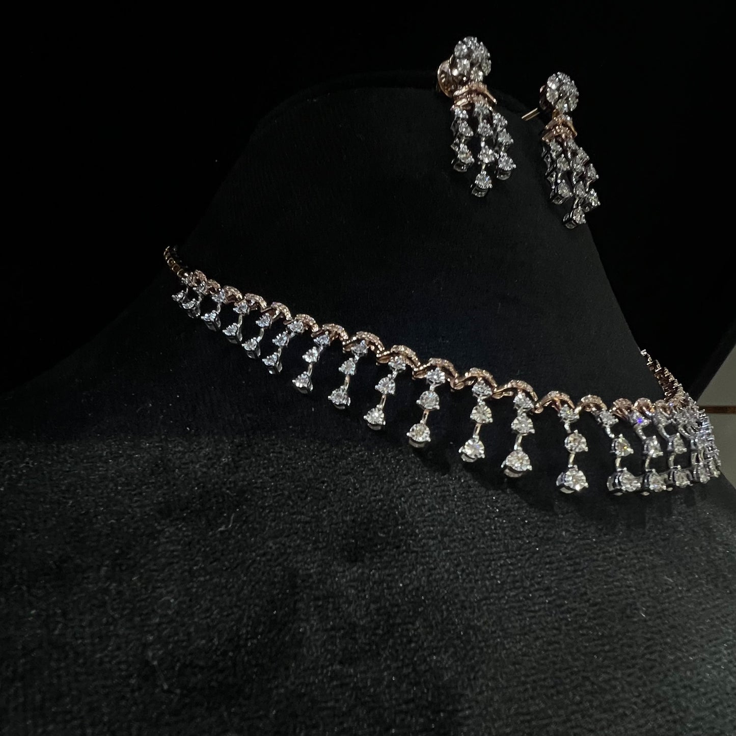 A gold diamond necklace with a series of round and marquise shaped earrings attached to the neckline, set on a black mannequin.