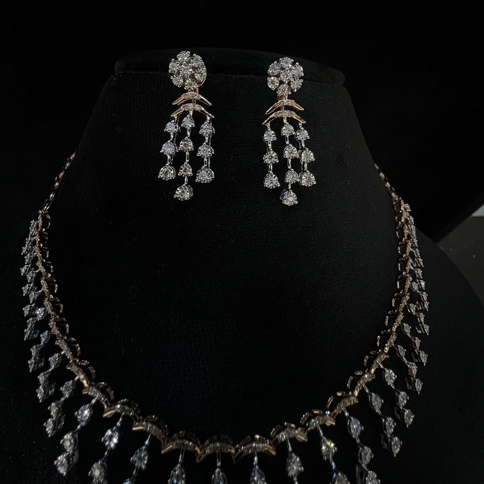 A gold diamond necklace with a series of round and marquise shaped earrings attached to the neckline, set on a black mannequin.