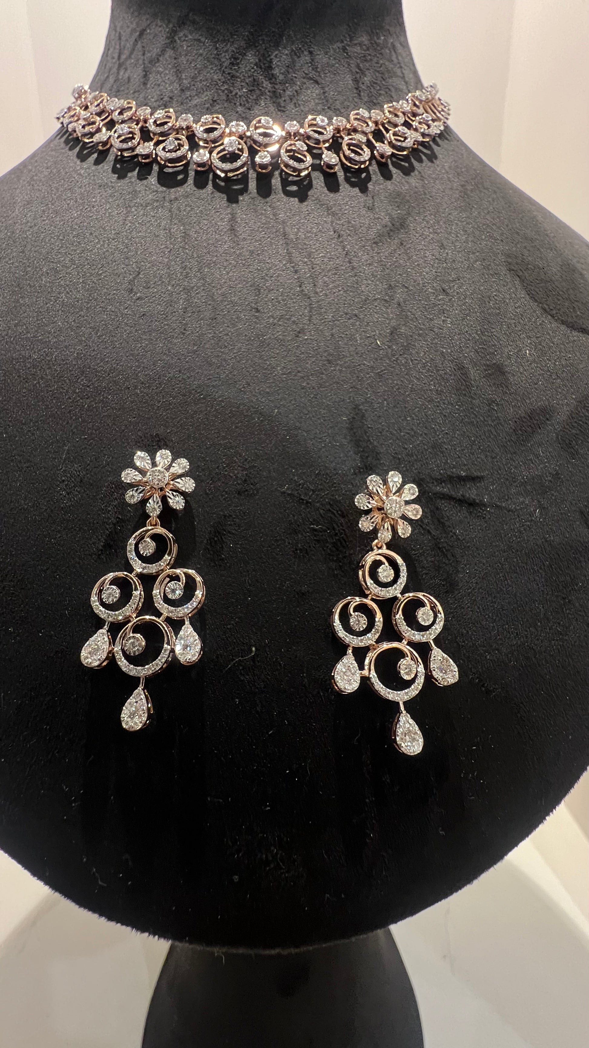 A gold diamond necklace and earrings set displayed on a mannequin bust, featuring a floral design with intricate detailing and adorned with genuine diamonds.