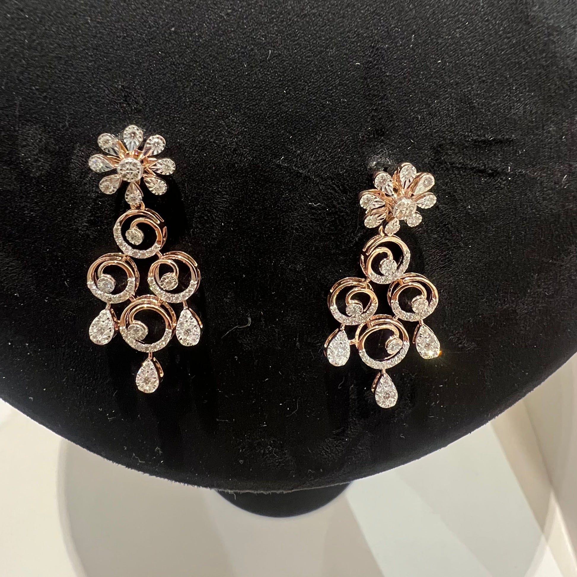 gold diamond earrings displayed on a mannequin bust, featuring a floral design with intricate detailing and adorned with genuine diamonds.