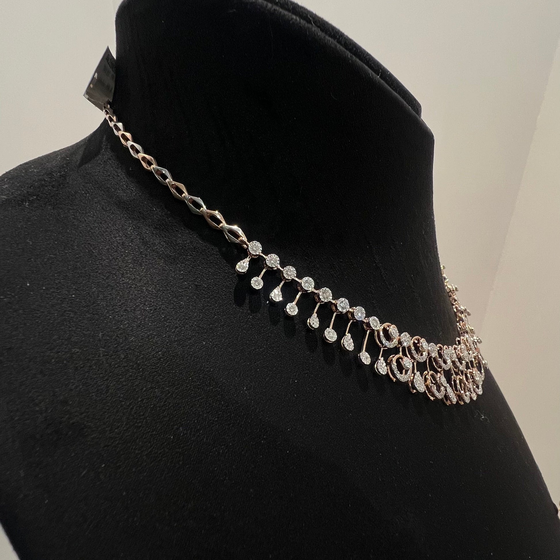 A gold diamond necklace displayed on a mannequin bust, featuring a floral design with intricate detailing and adorned with genuine diamonds.
