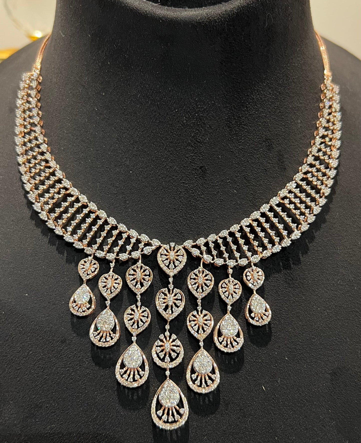 A gold diamond necklace with a geometric pattern and a pair of matching earrings, displayed on a mannequin bust.