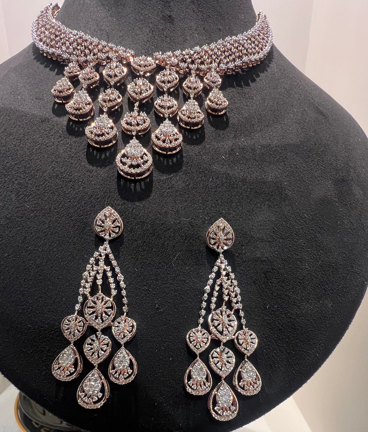 A gold diamond necklace with a geometric pattern and a pair of matching earrings, displayed on a mannequin bust.