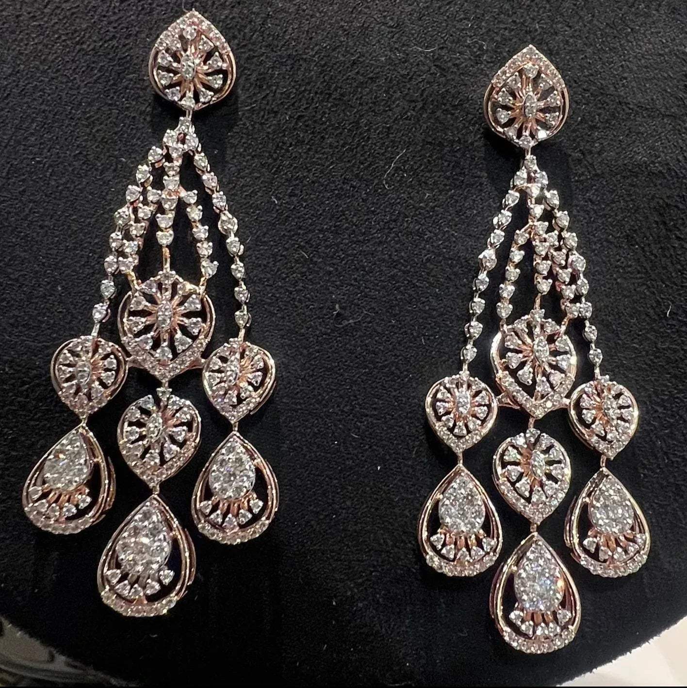 A pair of gold diamond earrings with a geometric pattern, displayed on a mannequin bust.