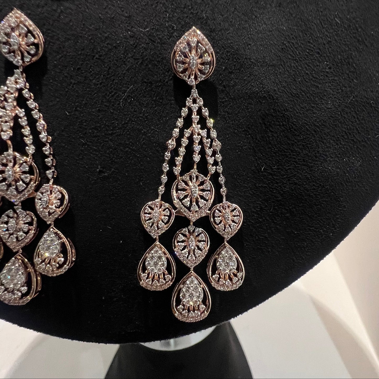A pair of gold diamond earrings, displayed on a mannequin bust.