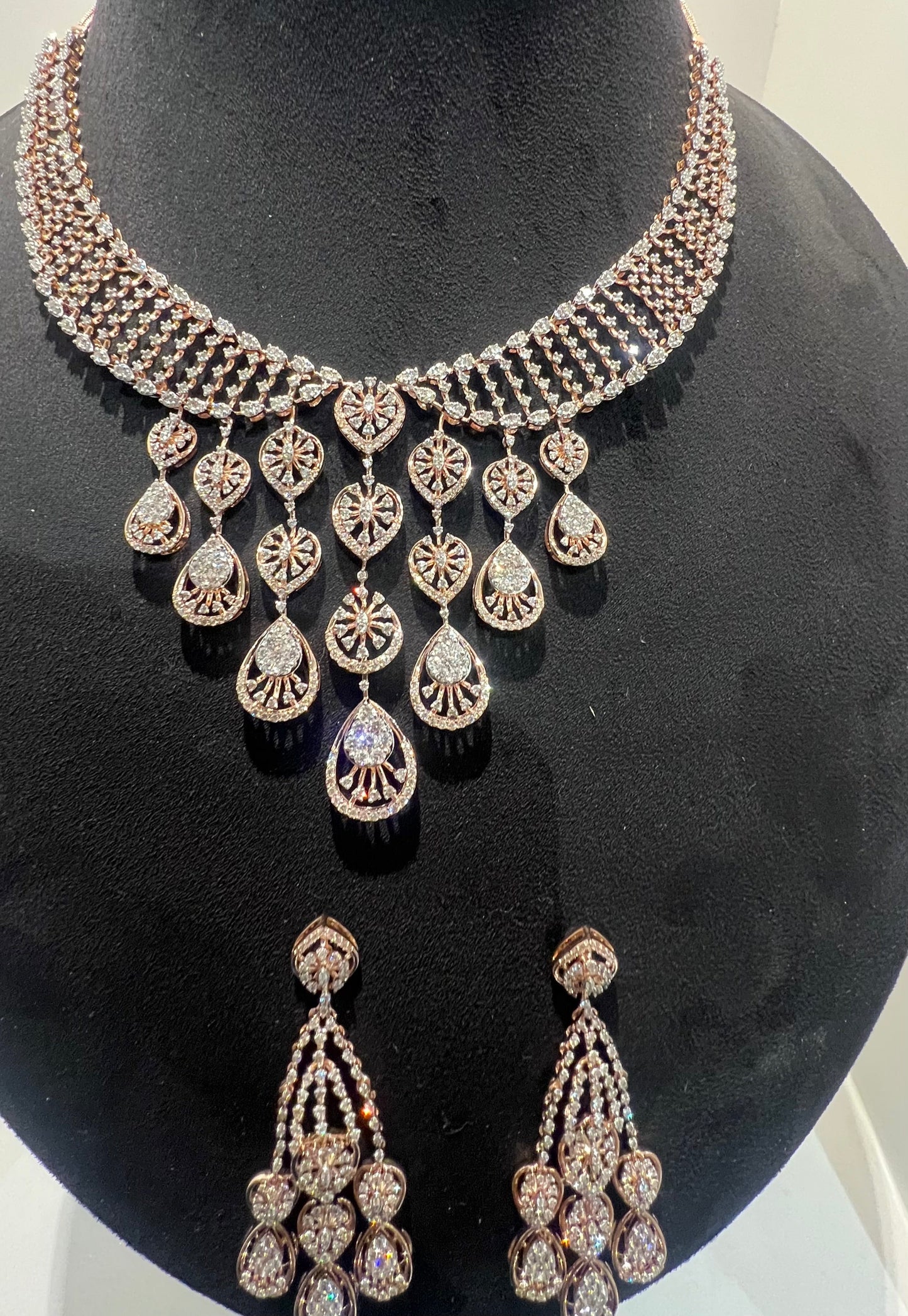 A gold diamond necklace with a geometric pattern and a pair of matching earrings, displayed on a mannequin bust.