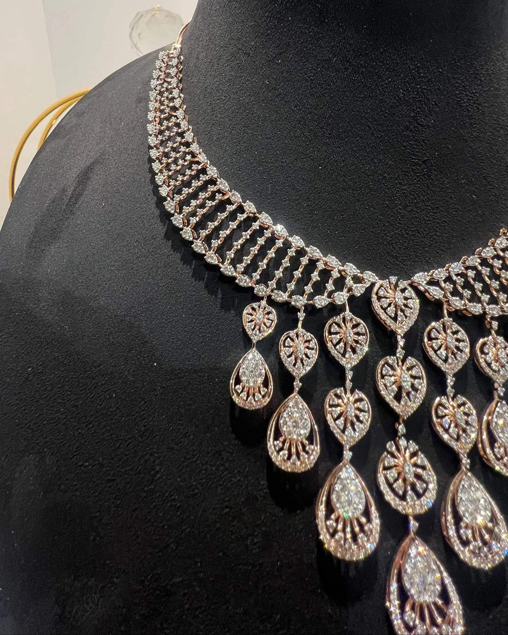 A gold diamond necklace with a geometric pattern, displayed on a mannequin bust.
