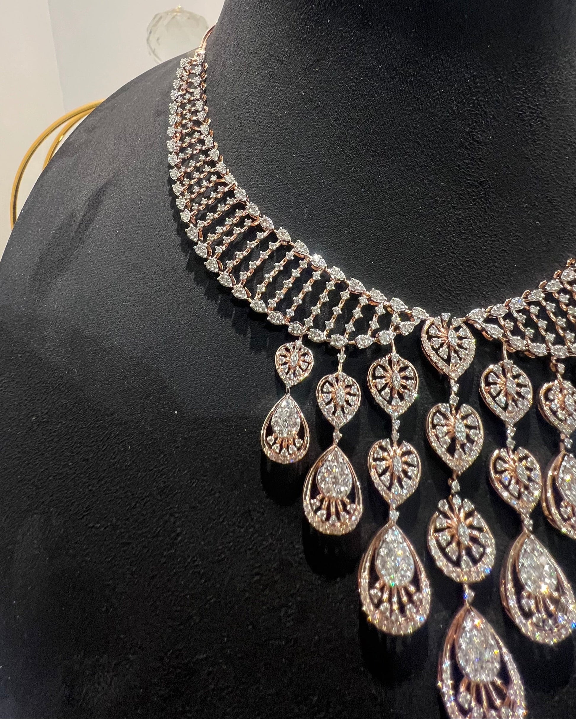 A gold diamond necklace with a geometric pattern, displayed on a mannequin bust.